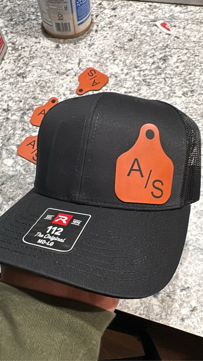 Black trucker hat with an orange cattle ear-tag style patch by KB Custom Creations