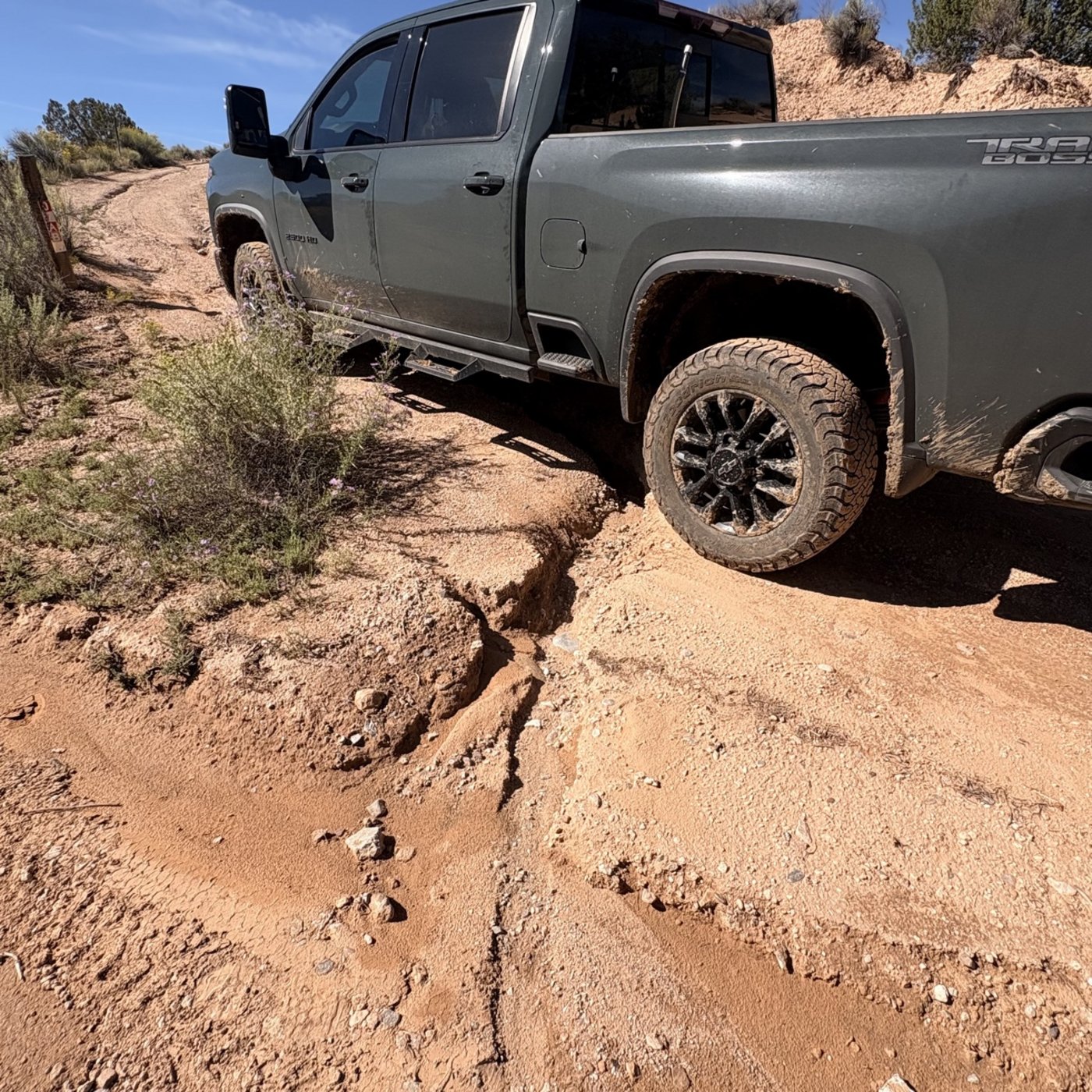 Work truck straddling the deep erosion rut in the dirt road, showing the scale of the washout damage