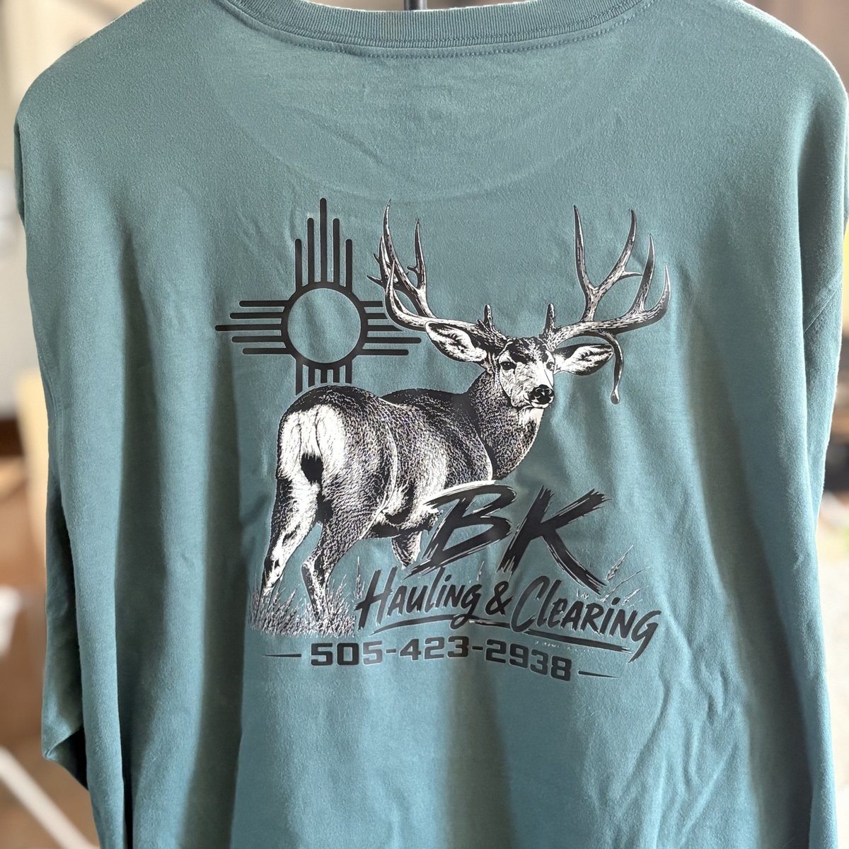 Teal long-sleeve shirt with a deer and Zia design for BK Hauling & Clearing, made by KB Custom Creations