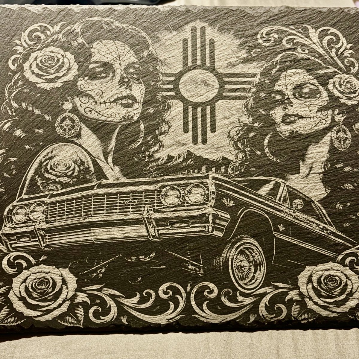 Engraved slate artwork with Día de los Muertos figures, a lowrider, roses, and a Zia symbol, by KB Custom Creations
