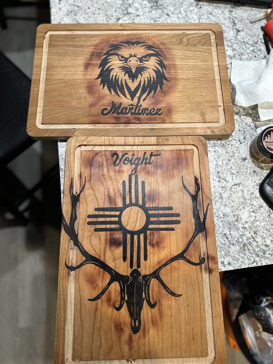 Two personalized engraved wood cutting boards — an eagle with a family name and a Zia with an elk skull — by KB Custom Creations