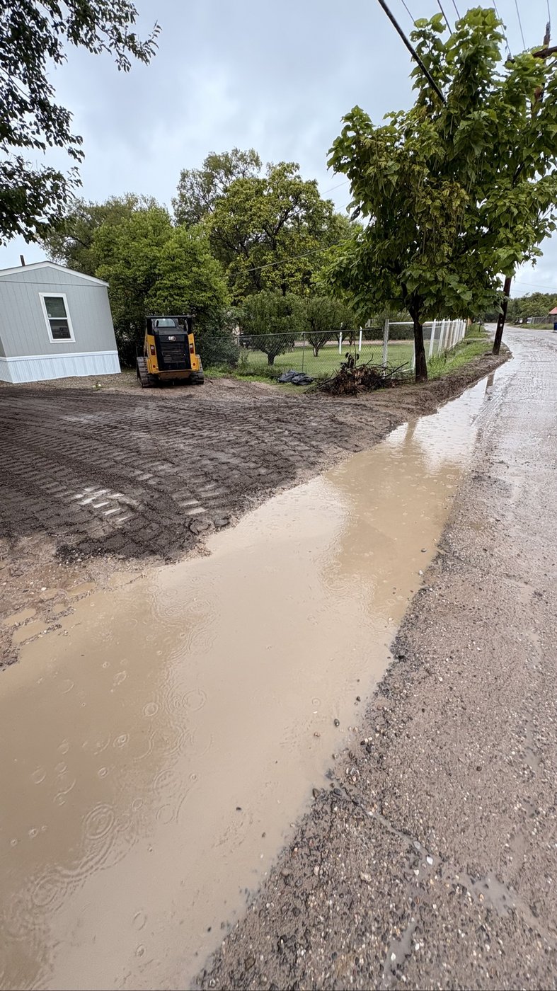 Street view of the finished job — graded lot with rainwater running along the road edge instead of flooding the property